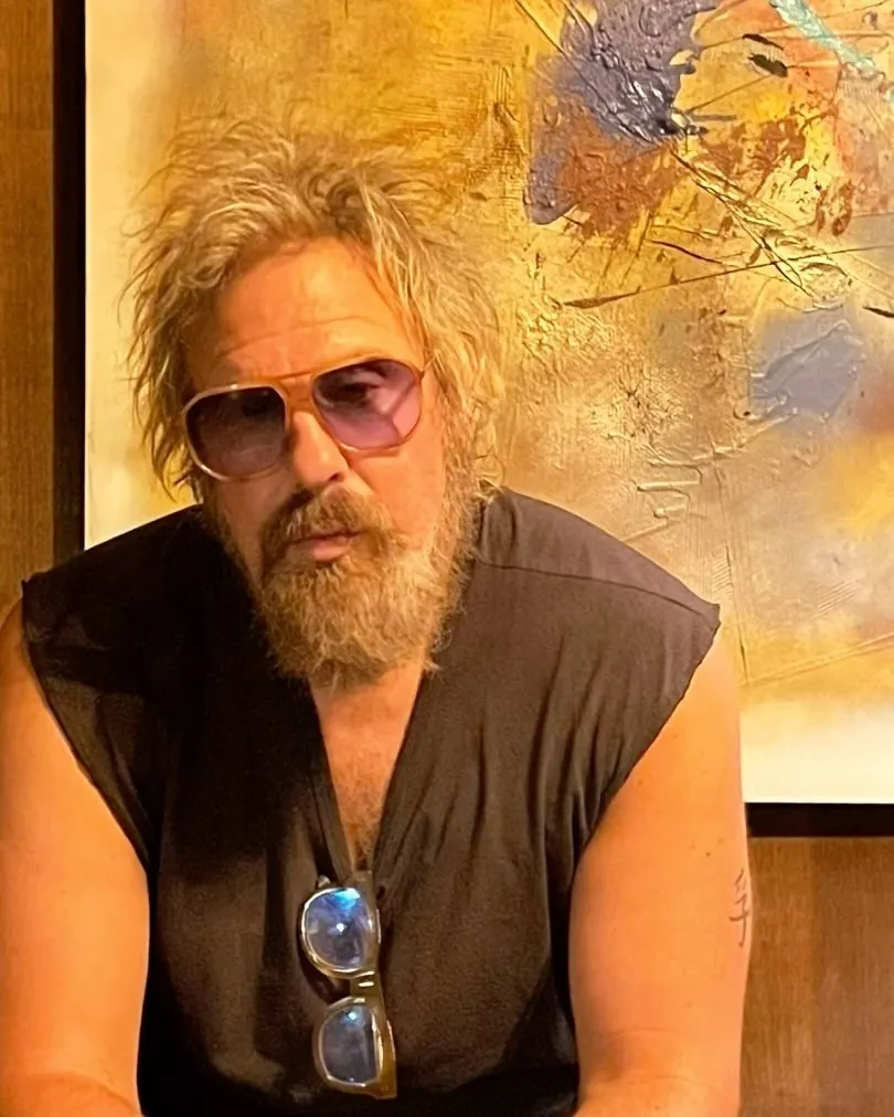 Brad Byrd in tinted glasses and a black sleeveless shirt, seated in front of an abstract painting