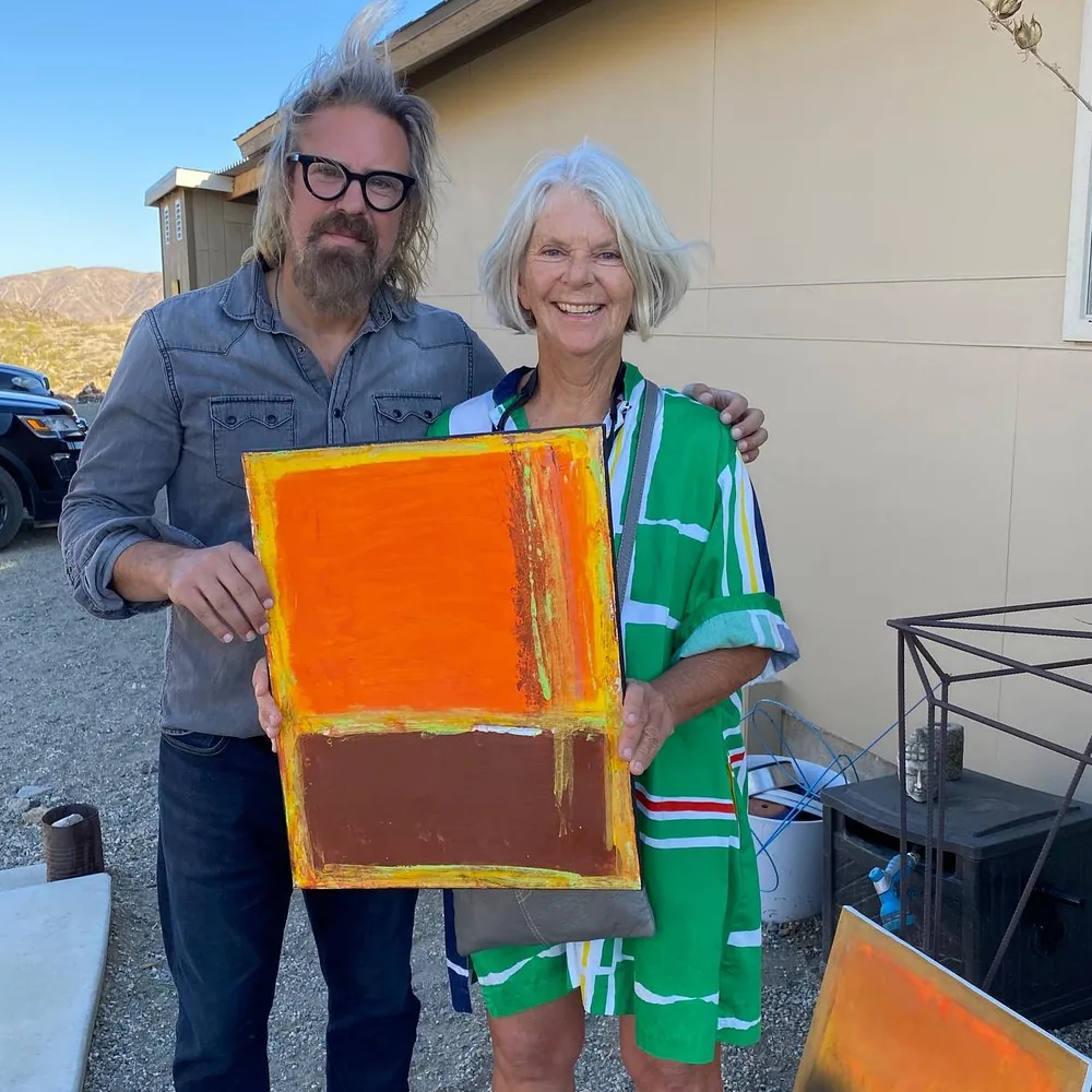 Brad Byrd with a smiling guest holding one of his orange paintings at Moon Rock Ranch during the Hwy 62 Art Tours