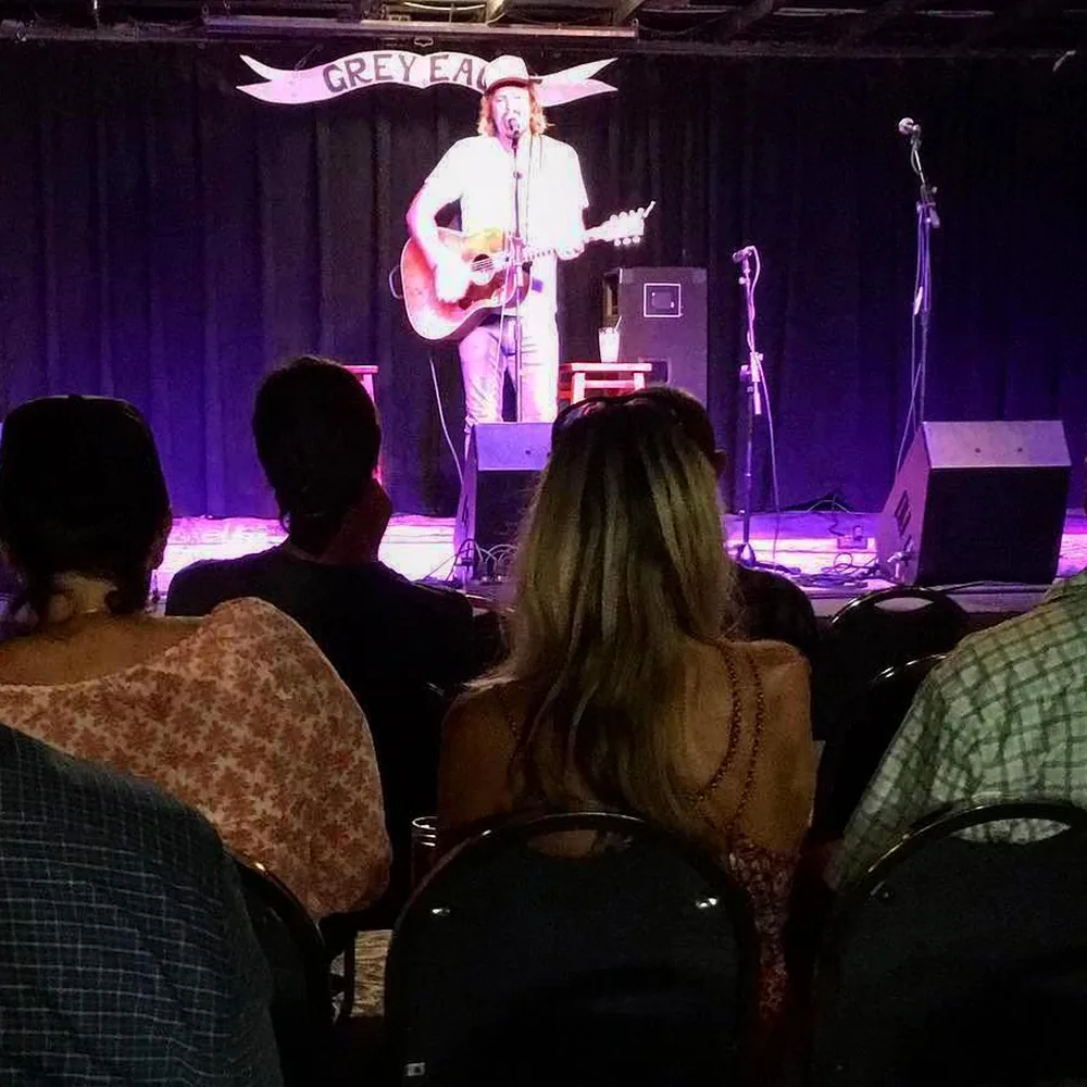 Guests in rows of chairs watching Brad Byrd play acoustic guitar on stage at The Grey Eagle in Asheville
