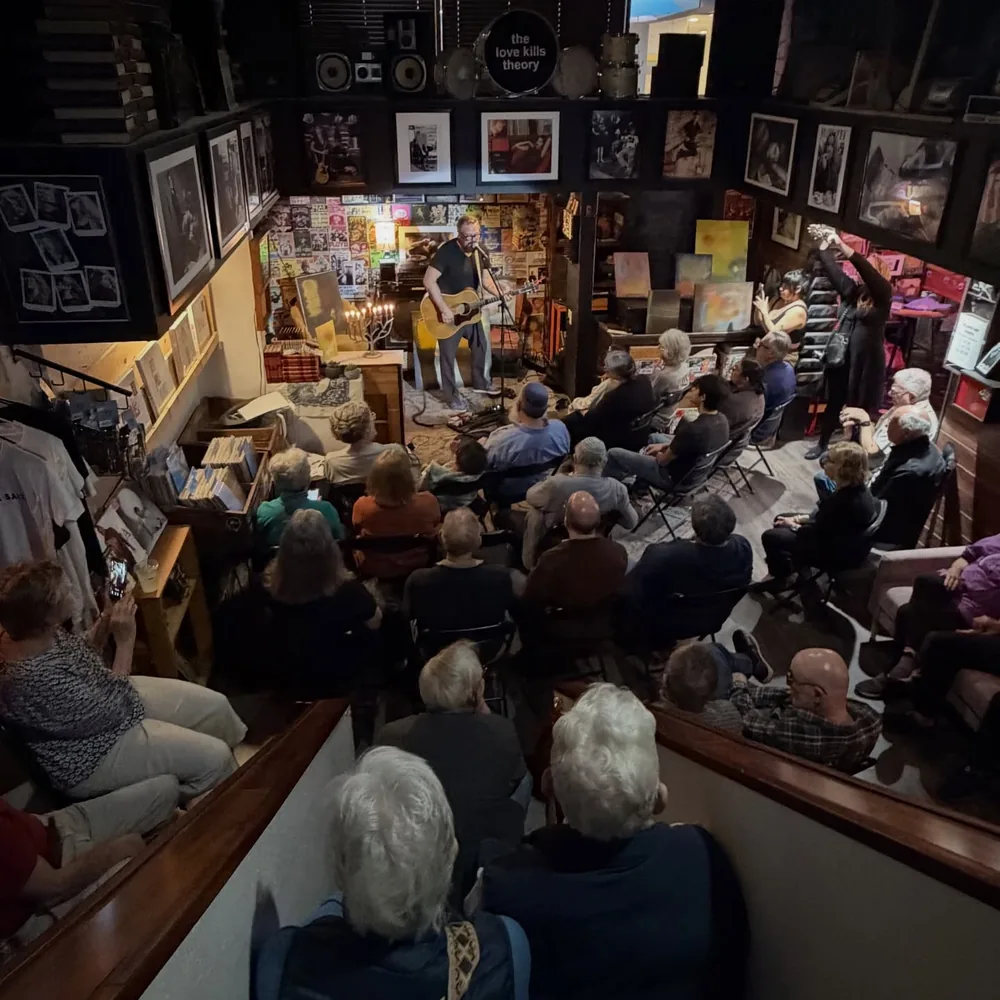 A packed seated crowd watching Brad Byrd play acoustic guitar at GRE Records and Coffee